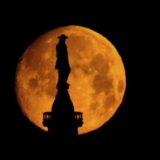 The moon sets behind a statue of William Penn atop of City Hall in Philadelphia, Wednesday, March 16, 2022.